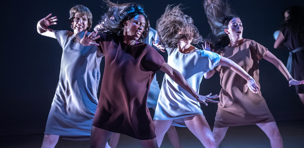 Four women in movement under stage lights.