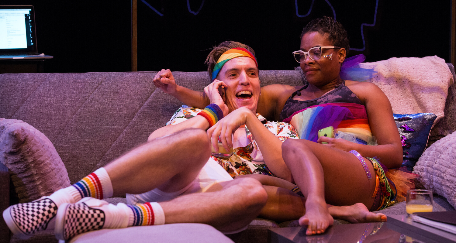 Adrian Shepherd-Gawinski and Monice Peter on the couch wearing rainbow clothing. Stage photo.