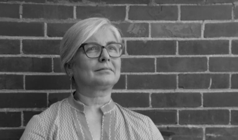 Shahrzad Arshadi in front of a brick wall. Black and white photo.