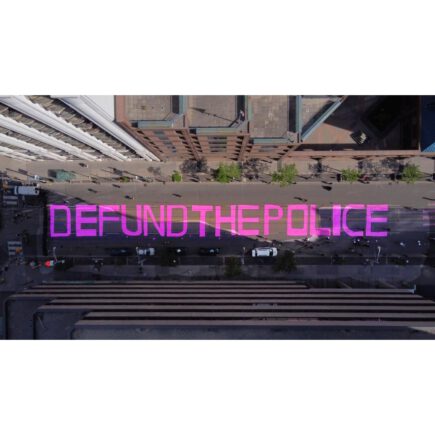 Aerial view of a street with "Defund the police" painted in pink letters.
