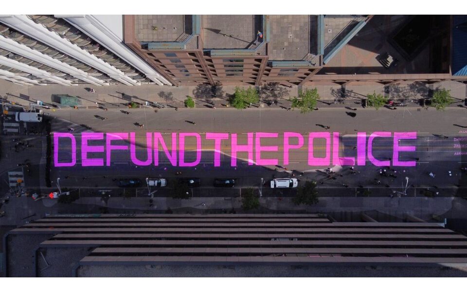 Aerial view of a street with "Defund the police" painted in pink letters.