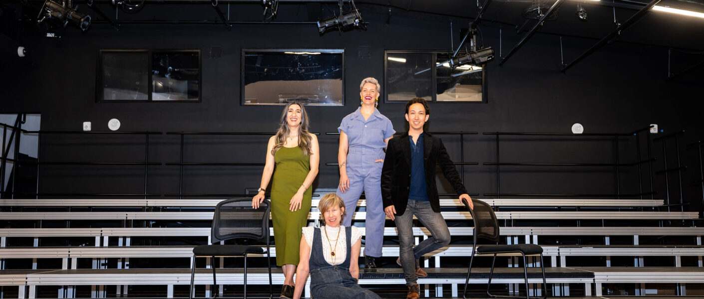 A photo of four people standing on risers in a theatre