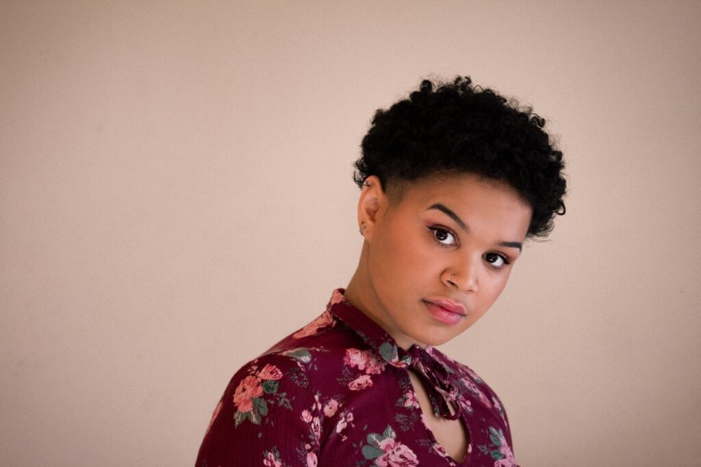photo of a black person in their 20s. they are wearing a maroon floral shirt and have short curly hair.