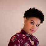 photo of a black person in their 20s. they are wearing a maroon floral shirt and have short curly hair.