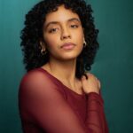 photo of a Caribbean woman in her 20s. she has curly dark hair and is wearing a sheer maroon top.