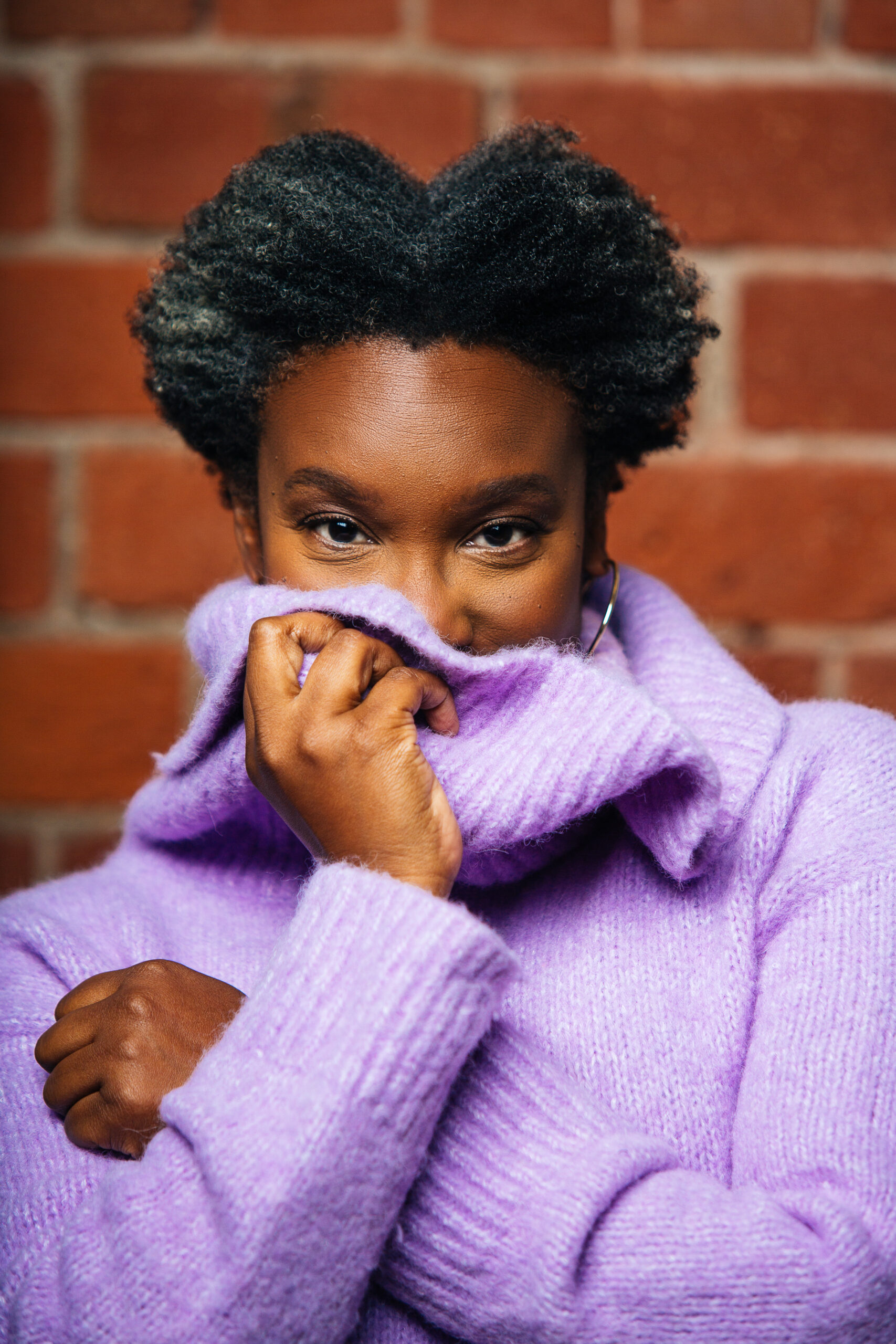 Headshot of Andrea Scott, covering the lower part of her face with a the oversized collar of lavender sweater.