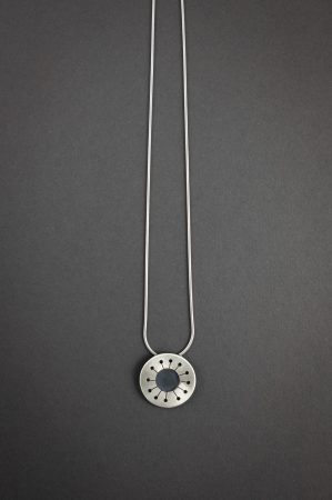 Against a grey background is a necklace that has a circular with a hole in the center, and 12 branches to much smaller holes coming off of the center.